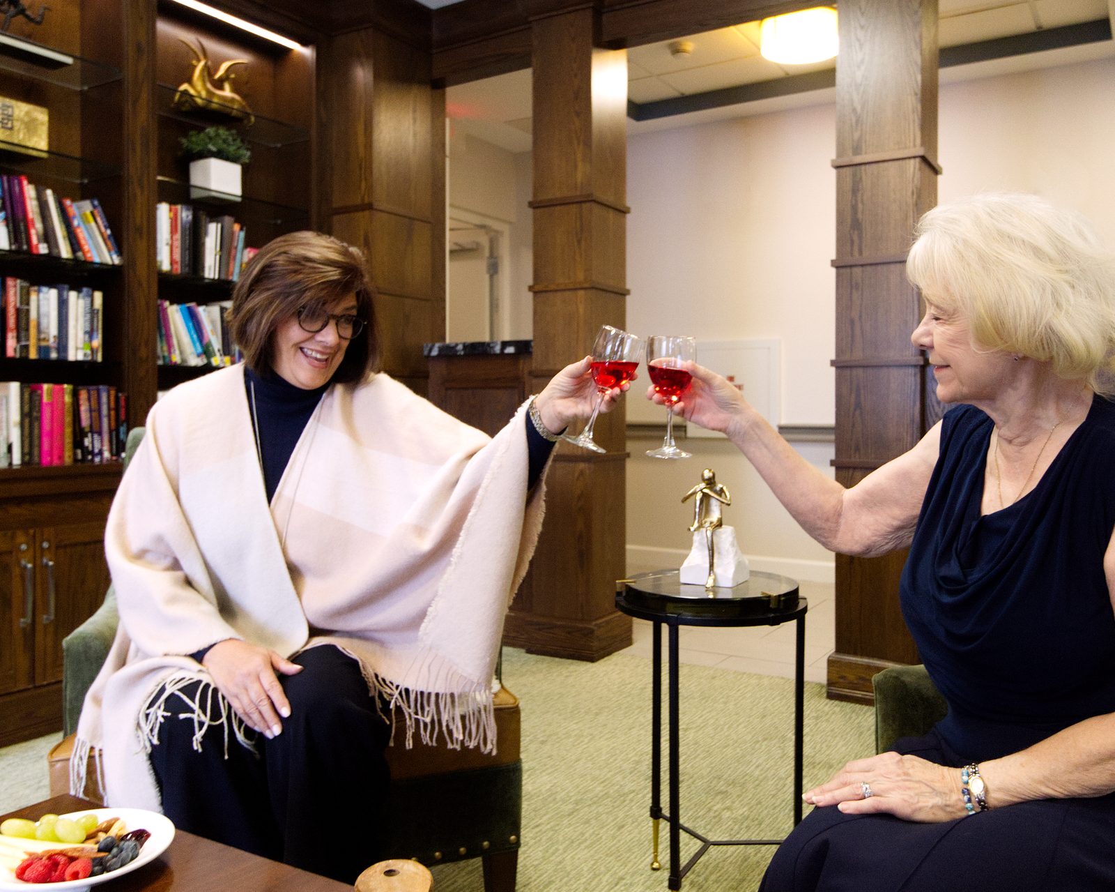 Two women sharing a toast with wine glasses in the Evolve at Lake Zurich library lounge