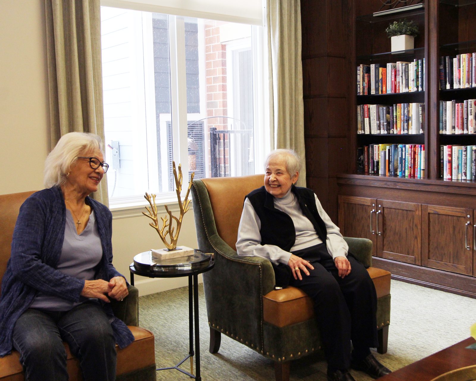 Two residents chatting together in the Evolve at Lake Zurich library lounge
